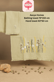 Set of green towels with floral embroidery on a brown background, featuring Aavva Homes branding.