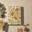 Floral-patterned pouch, bottle, and box on a beige surface with scattered flowers.